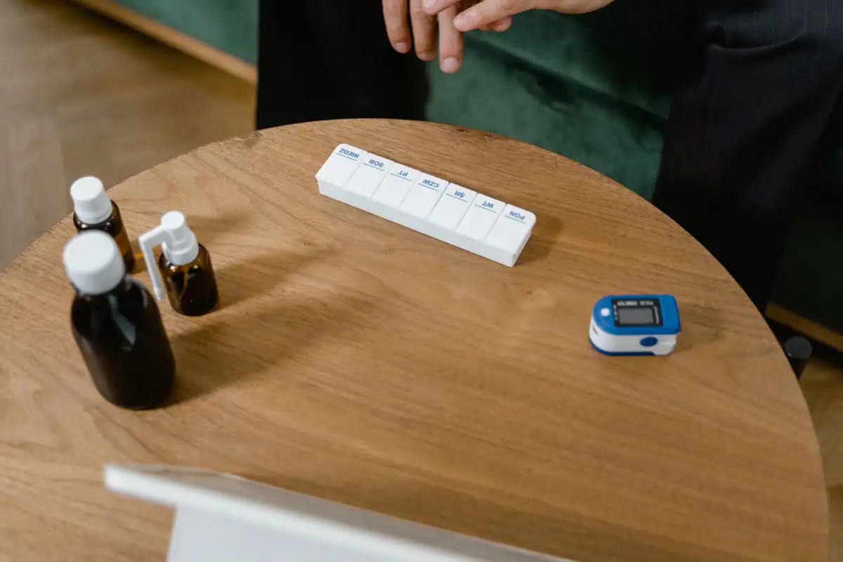 Pastilier săptămânal, flacoane cu medicamente și pulsoximetru pe o masă de lemn