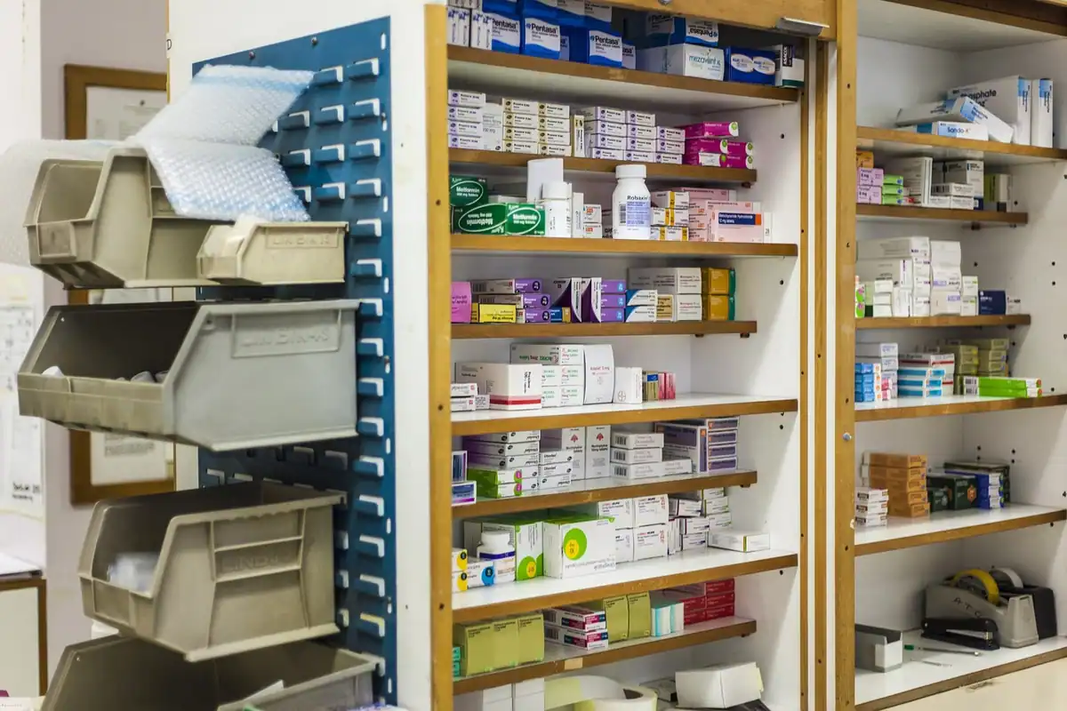 Rafturi de farmacie cu cutii de medicamente aranjate pe categorii și sertare etichetate