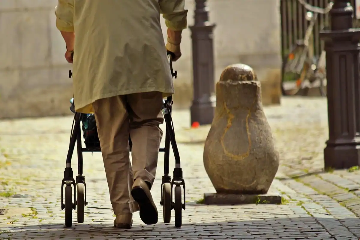 Persoană în vârstă care merge pe stradă sprijinită de un cadru de mers
