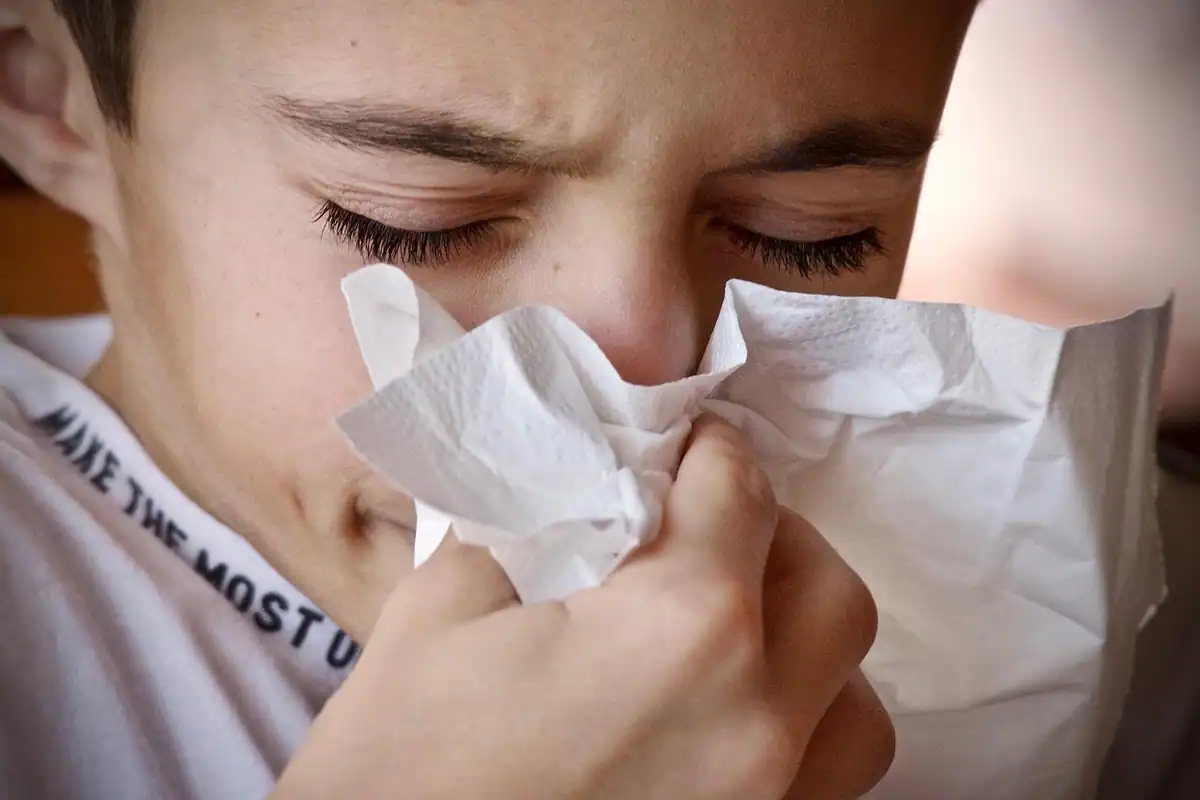 Băiat cu fața strânsă care își suflă nasul într-un șervețel de hârtie