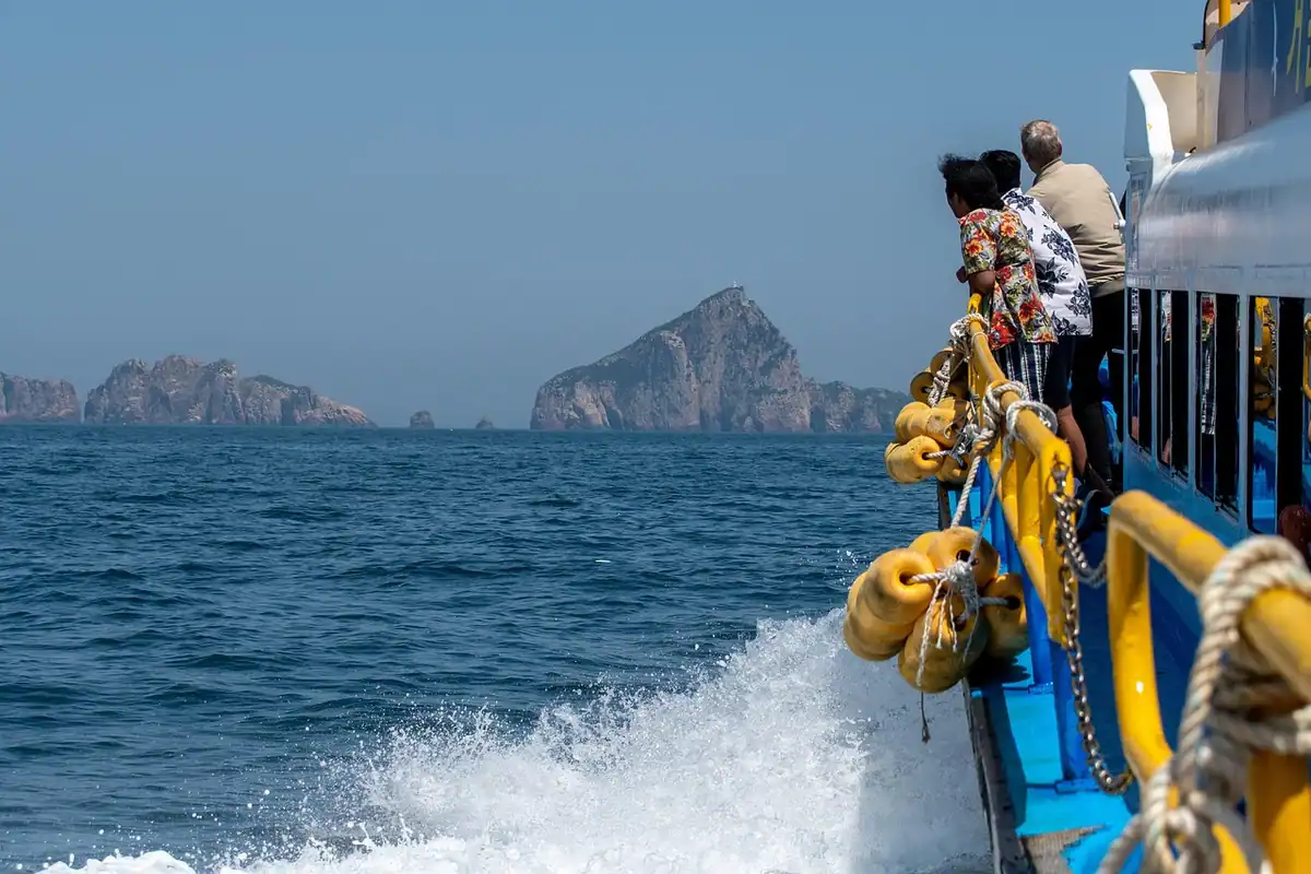 Valuri făcute de o navă în mers, cu pasageri la bord și o stâncă în zare