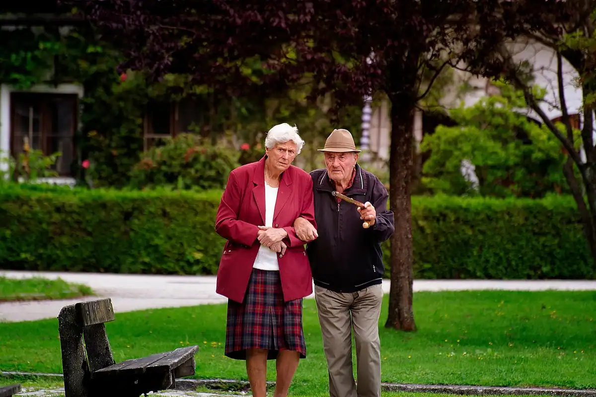 Cuplu de vârstnici care se plimbă sprijinindu-se unul de altul într-un parc verde