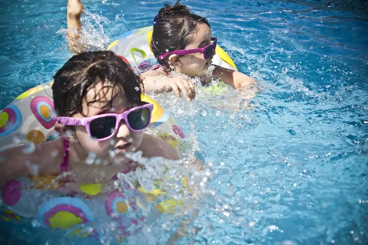 Două fetițe cu colaci și ochelari de înot care se joacă în piscină