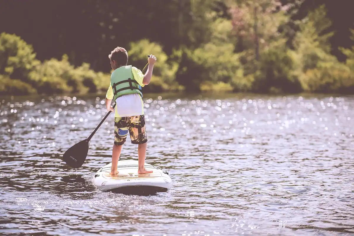 Băiat în vestă de salvare care stă pe o placă de paddle pe un lac