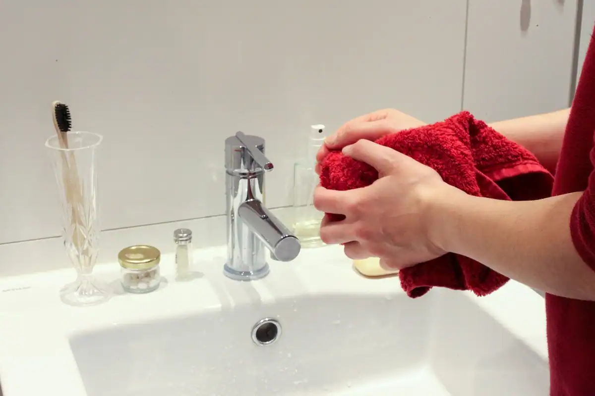 Persoană care își șterge mâinile cu un prosop roșu lângă chiuveta albă din baie
