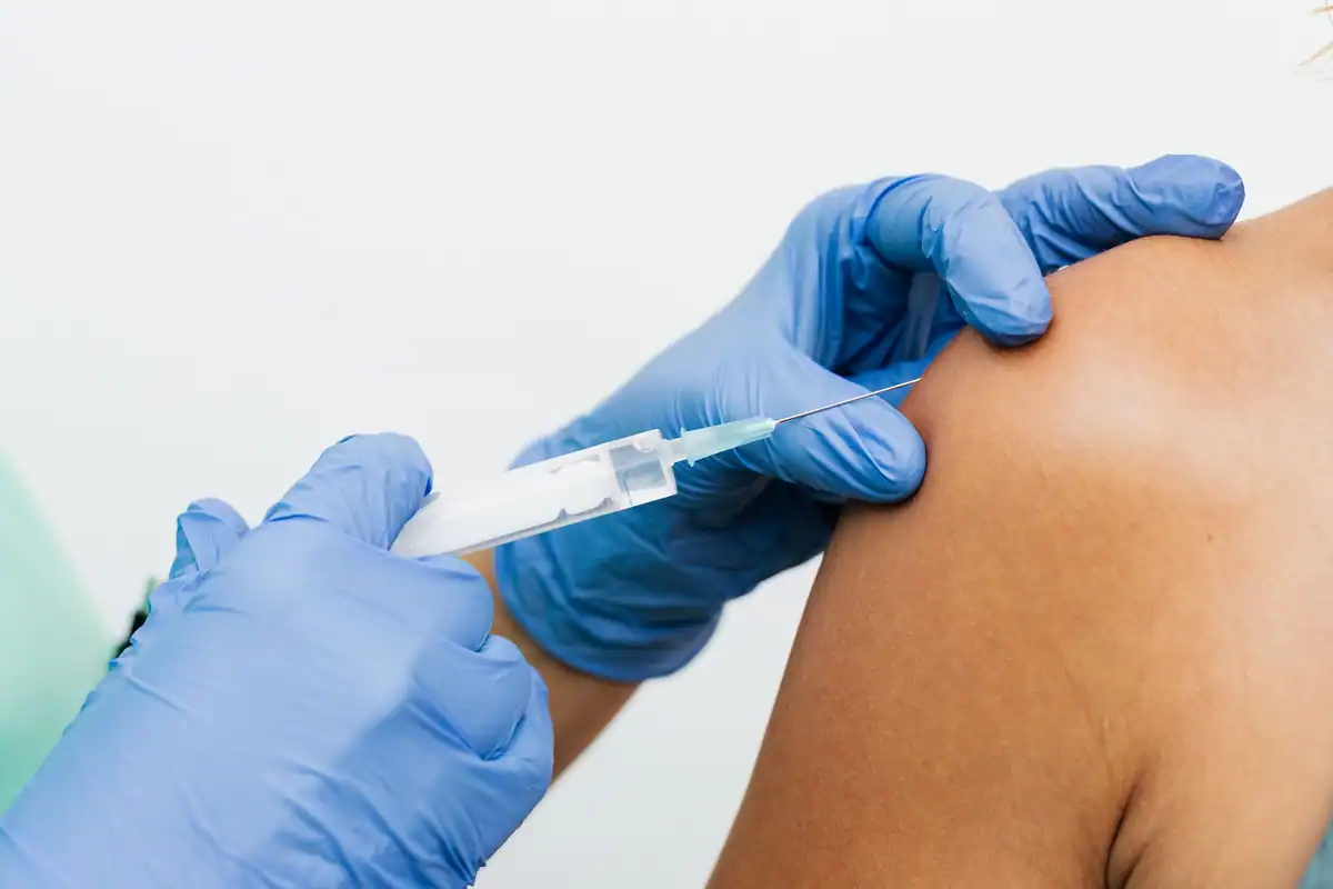 Un cadru medical cu mănuși administrează o injecție în brațul unui pacient, în plan apropiat