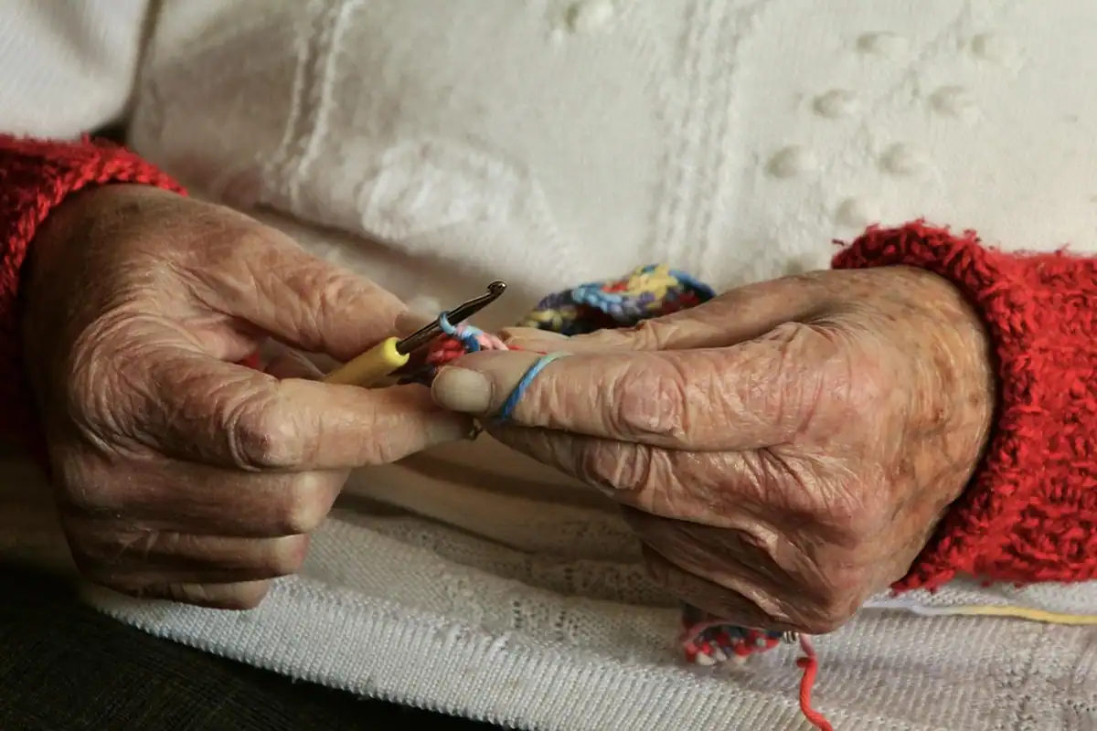 Mâini bătrâne care împletesc cu andrele, îmbrăcate într-un pulover călduros