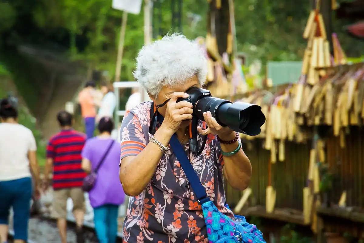 Femeie în vârstă care fotografiază cu un aparat foto, într-o excursie printre turiști
