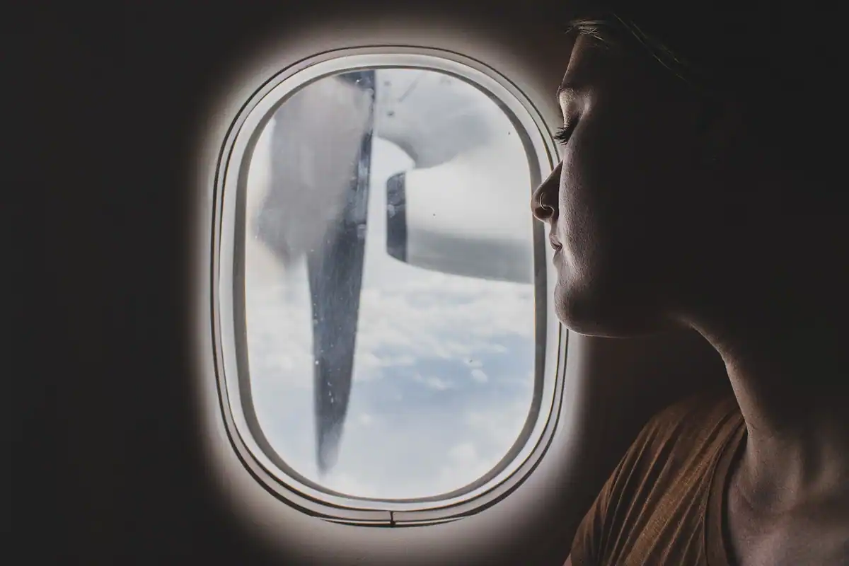 Femeie care privește pe hublou, în penumbra unei cabine de avion