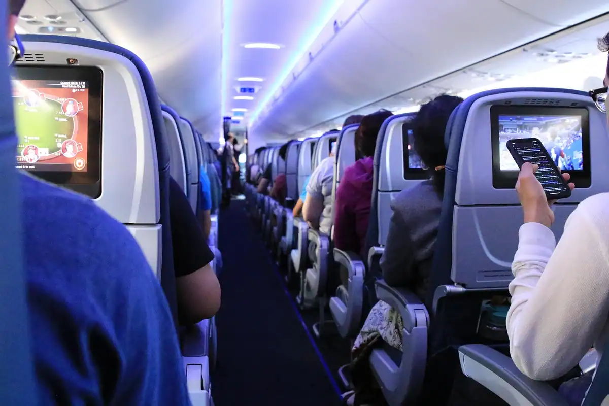 Culoar dintr-un avion de pasageri cu scaune ocupate și ecrane în spătare